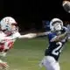 A football player in a blue jersey reaches for the ball while an opponent in a red jersey attempts to defend. — 58-32