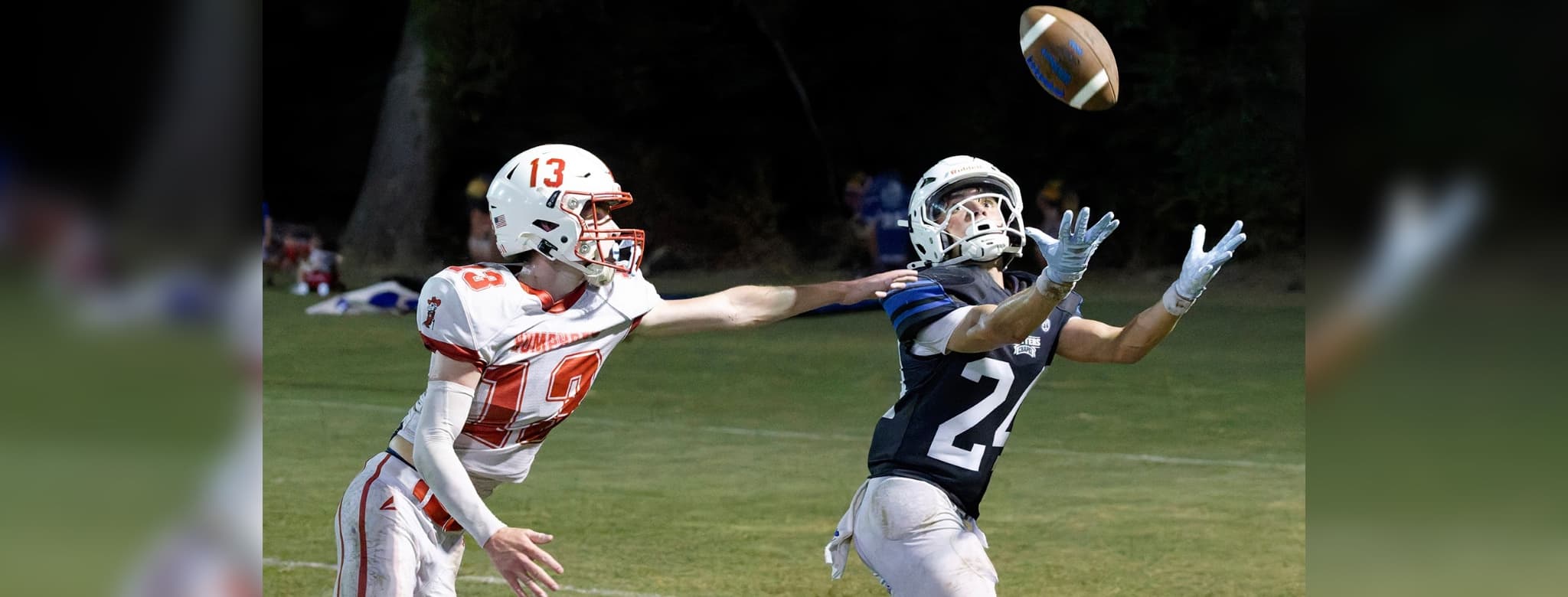 A football player in a blue jersey reaches for the ball while an opponent in a red jersey attempts to defend. — 58-32