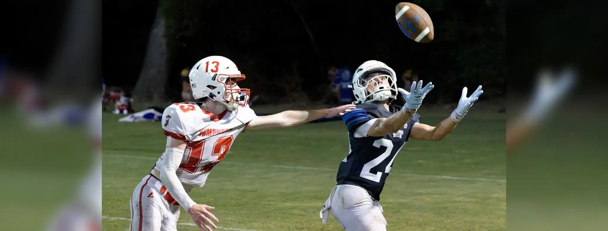 A football player in a blue jersey reaches for the ball while an opponent in a red jersey attempts to defend. — 58-32