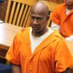 A man in an orange prison jumpsuit stands in a courtroom, looking serious, with other individuals se — Failure to register