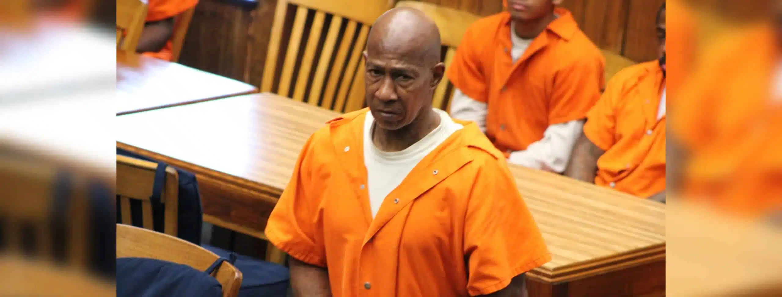 A man in an orange prison jumpsuit stands in a courtroom, looking serious, with other individuals se — Failure to register