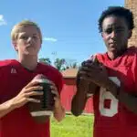 Two young football players in red jerseys, one holdin — Morgan throws three touchdowns; Miles scores four in WCJHS victory