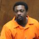 A man in an orange jumpsuit appears in a courtroom setting, looking serious. — $5 million