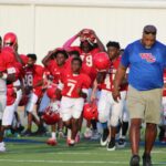 Warren Central Junior High's seventh-grade football team runs onto the field, wearing red jerseys and helmets, with coache…