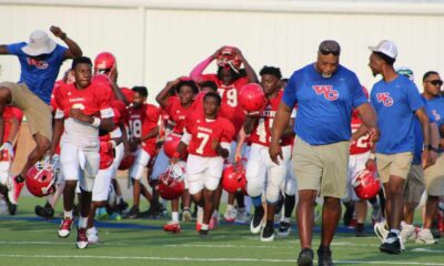 Warren Central Junior High's seventh-grade football team runs onto the field, wearing red jerseys and helmets, with coache…