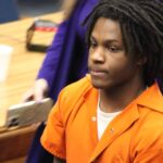 An 18-year-old in an orange jumpsuit sits in a courtroom, looking serious during sentencing. — 18 year old