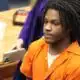 An 18-year-old in an orange jumpsuit sits in a courtroom, looking serious during sentencing. — 18 year old