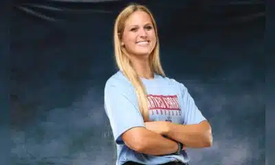 A confident volleyball player in a blue shirt stands with arms crossed, smiling against a dark background. — Sweeps canton