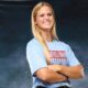A confident volleyball player in a blue shirt stands with arms crossed, smiling against a dark background. — Sweeps canton