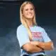 A confident volleyball player in a blue shirt stands with arms crossed, smiling against a dark background. — Sweeps canton