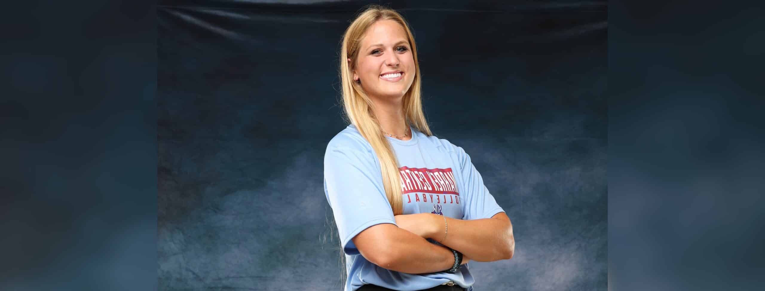 A confident volleyball player in a blue shirt stands with arms crossed, smiling against a dark background. — Sweeps canton