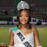 Lauren Gibbs wearing a crown and sash, smiling while holding flowers on a football field.