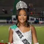 Lauren Gibbs wearing a crown and sash, smiling while holding flowers on a football field.