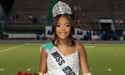 Lauren Gibbs wearing a crown and sash, smiling while holding flowers on a football field.