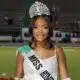 Lauren Gibbs wearing a crown and sash, smiling while holding flowers on a football field.