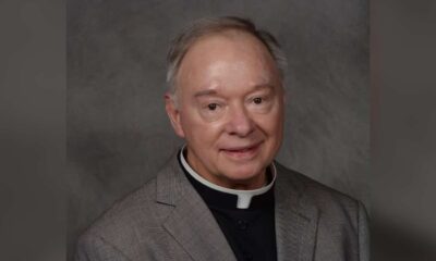 Father Robert Dore, a priest in a gray suit with a clerical collar, smiling softly at the camera.