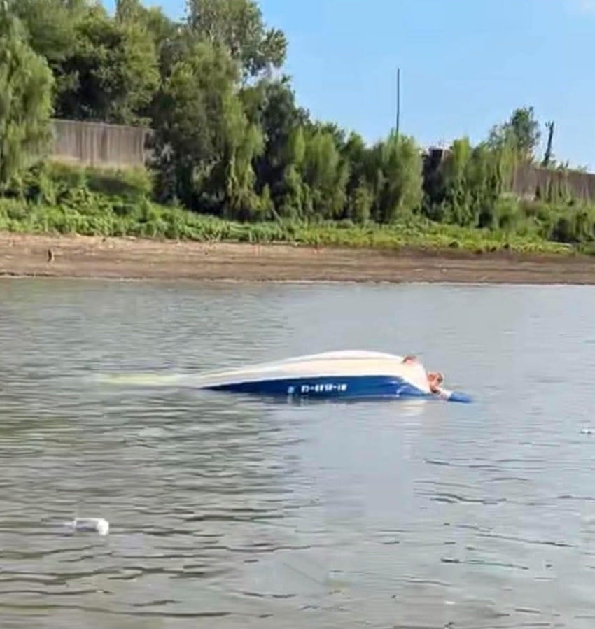 Capsized ski boat on the river with visible damage and water surrounding it. — Barge