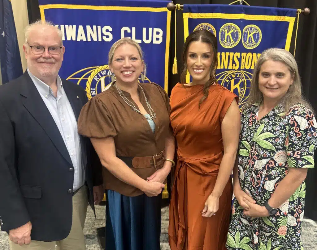 Four individuals posing together at a Kiwanis Club event with banners in the background.