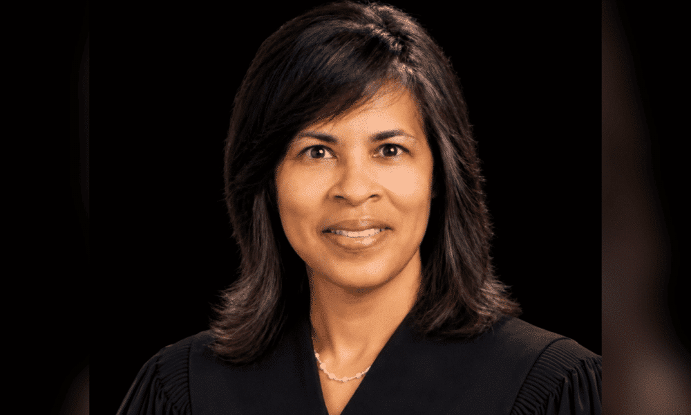 Judge Vicki Barnes in judicial robes, smiling against a dark background. — Caseload split following Judge Barnes passing