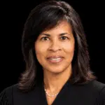 Judge Vicki Barnes in judicial robes, smiling against a dark background.