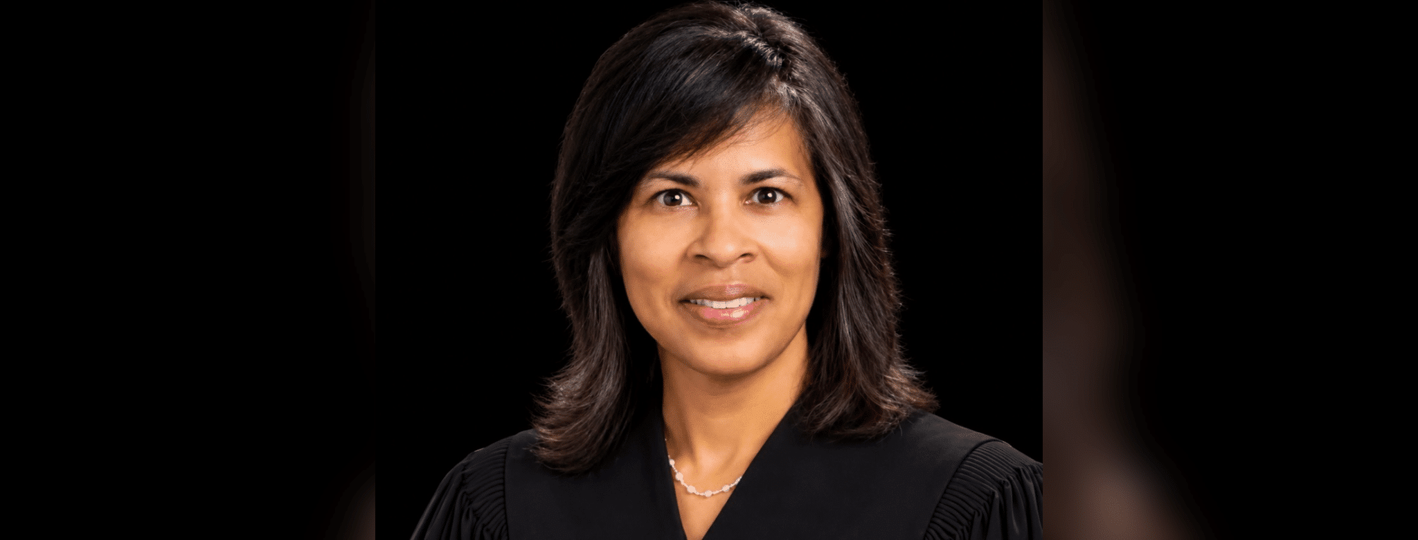 Judge Vicki Barnes in judicial robes, smiling against a dark background.