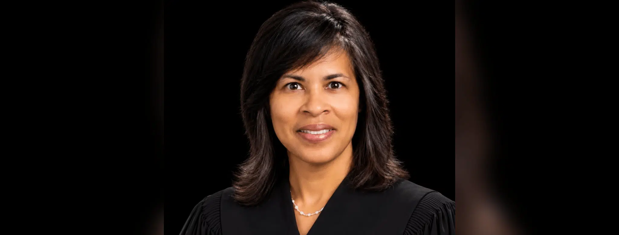 Judge Vicki Barnes in judicial robes, smiling against a dark background.