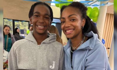 Teen with a genetic disorder smiles beside a woman at an indoor gathering with green and blue balloons.
