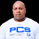 William Prince, a former athlete, wearing a white shirt with PCS logo, looking serious and confident.