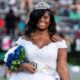 Jenieve Moorehead wearing a crown and white dress, smiling while holding a bouquet at a football game.