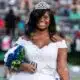 Jenieve Moorehead wearing a crown and white dress, smiling while holding a bouquet at a football game.
