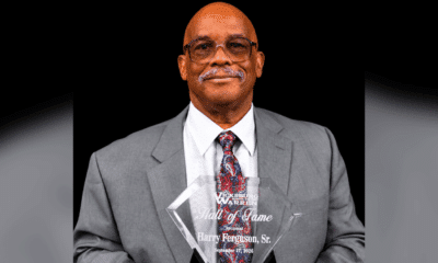 Harry Ferguson Sr. holding his Hall of Fame award, dressed in a gray suit with a patterned tie.