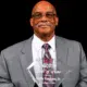 Harry Ferguson Sr. holding his Hall of Fame award, dressed in a gray suit with a patterned tie.