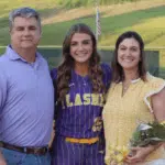 Megan Theriot in a softball uniform poses with her parents on t — Megan Theriot selected to play in the MAIS All-Star Game