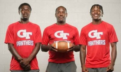 Three coaches in red shirts holding a football, standing together in a sports set — Devonte Cage and Laurence Sullivan Jr.