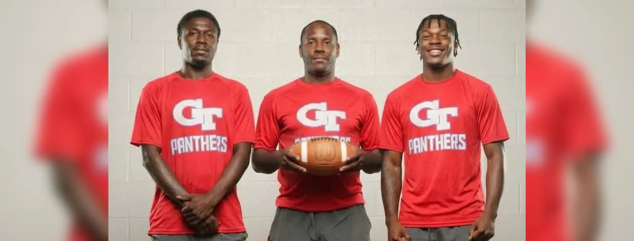 Three coaches in red shirts holding a football, standing together in a sports set — Devonte Cage and Laurence Sullivan Jr.