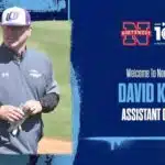 David Kuhn in a gray jacket and baseball cap, smiling on a softball field.