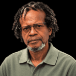 A serious-looking man with glasses and curly hair, wearing a green polo shirt. — Leroy Newton