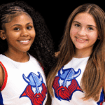 Two young cheerleaders smiling, wearing cheer uniforms with a Viking logo, celebrating their roles as cheer captains.