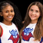Two young cheerleaders smiling, wearing cheer uniforms with a Viking logo, celebrating their roles as cheer captains.