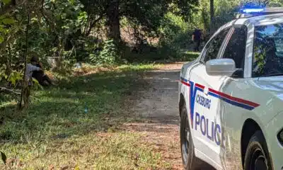 Police car with lights on near a wooded area where a person is seated on the ground, indicating a shoo — Shot in Vicksburg