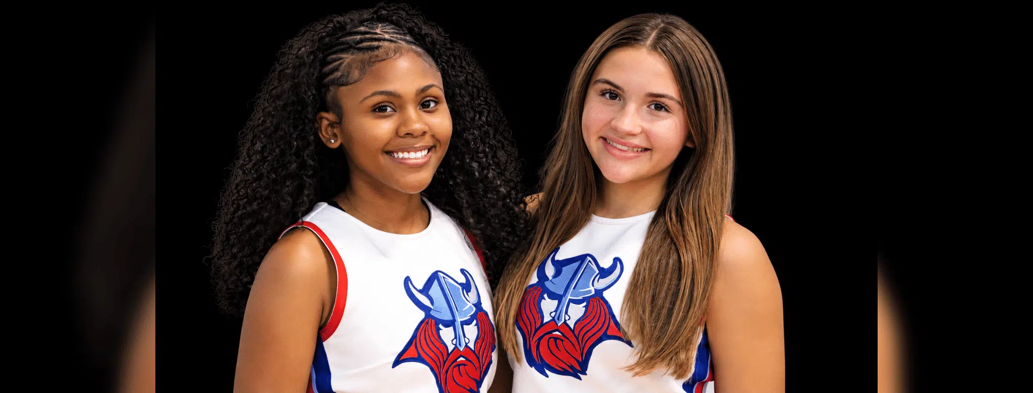 Two young cheerleaders smiling, wearing cheer uniforms with a Viking logo, celebrating their roles as cheer captains.
