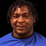 A 24-year-old man with dreadlocks wearing a blue shirt, smiling against a dark background. — 24 year old