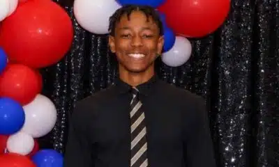 A smiling young man in a black shirt and tie stands in front of red, white, and blue balloons. — Henry Trisby III
