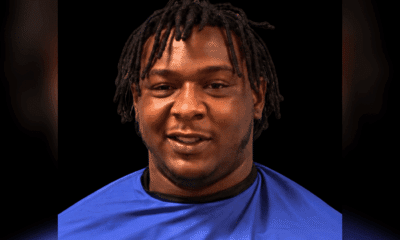 A 24-year-old man with dreadlocks wearing a blue shirt, smiling against a dark background. — 24 year old