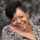 Smiling woman with short hair and a leopard print top, resting her chin on her hand against a textured background. — Verna