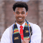 Kameren Batty smiles in a white shirt, red tie and colorful stole.