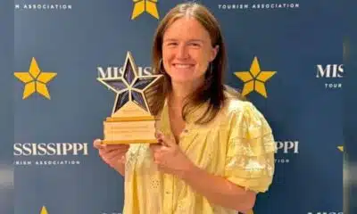 A woman in a yellow blouse holds a star-shaped award in front of a blue backdrop with Mississippi Tourism Associ — Anchuca