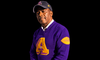 Ernest Young wearing a purple and gold sweater and dark cap against a black background