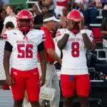 Four football players in red and white uniforms stand on the sidelines during a game. — Warren Central district play