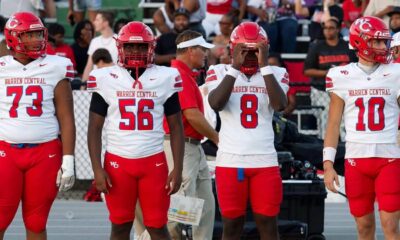 Four football players in red and white uniforms stand on the sidelines during a game. — Warren Central district play